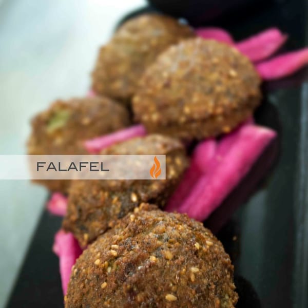 Close-up of golden-brown falafel balls garnished with bright pink pickled turnips on a dark plate.