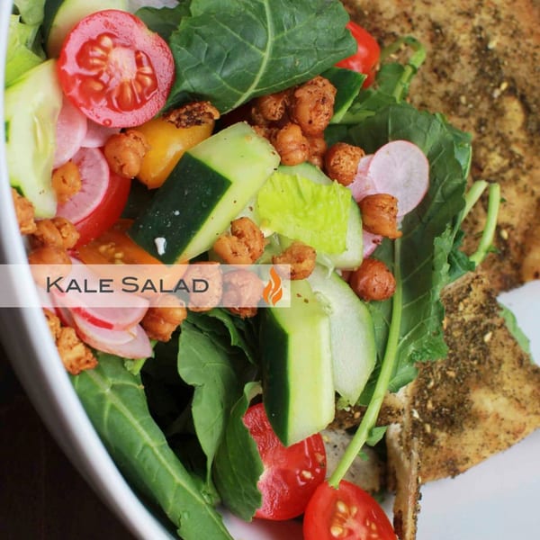 Close-up of a vibrant Byblos kale salad with chickpeas, tomatoes, cucumbers, and radishes.
