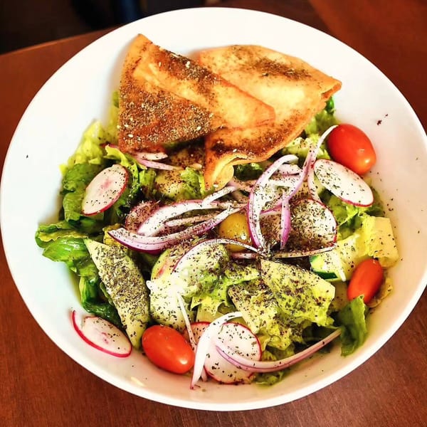 A vibrant Byblos Fattoush salad with lettuce, tomatoes, radishes, onions, and crispy pita bread.