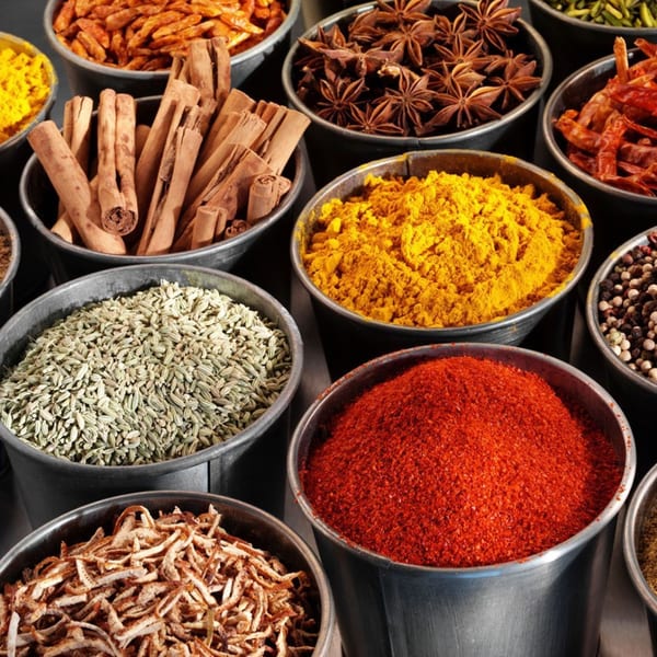 Various Mediterranean spices like cinnamon sticks, star anise, and colorful powders in metal bowls.