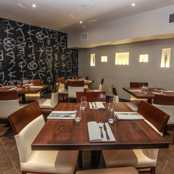 Byblos Mediterranean restaurant dining room with dark wood tables, white chairs, and a black wall with white symbols.