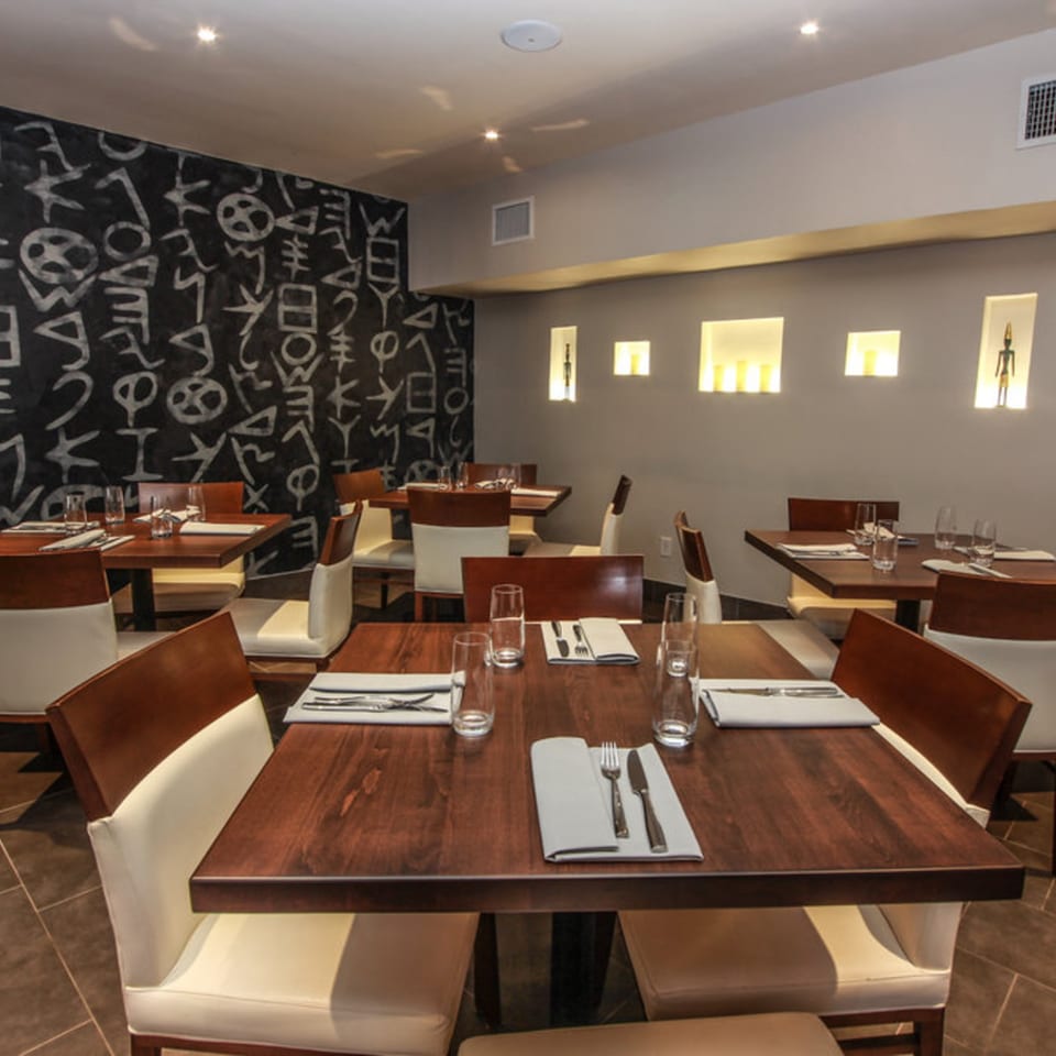 Byblos Mediterranean restaurant dining room with dark wood tables, white chairs, and a black wall with white symbols.