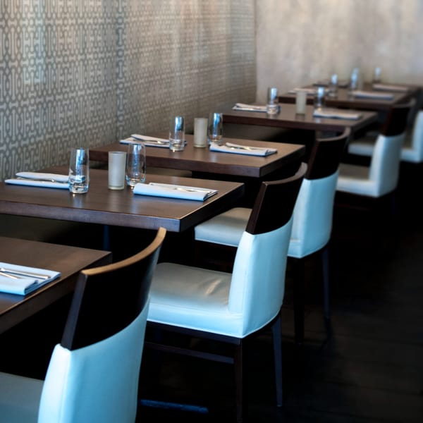 Byblos restaurant dining room with dark wooden tables, white chairs, and patterned wallpaper.