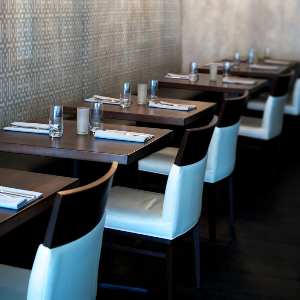 Byblos restaurant dining room with dark wooden tables, white chairs, and patterned wallpaper.