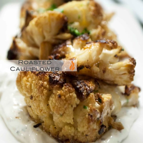 Close-up of roasted cauliflower florets with charred edges, garnished with herbs, on a creamy white sauce.