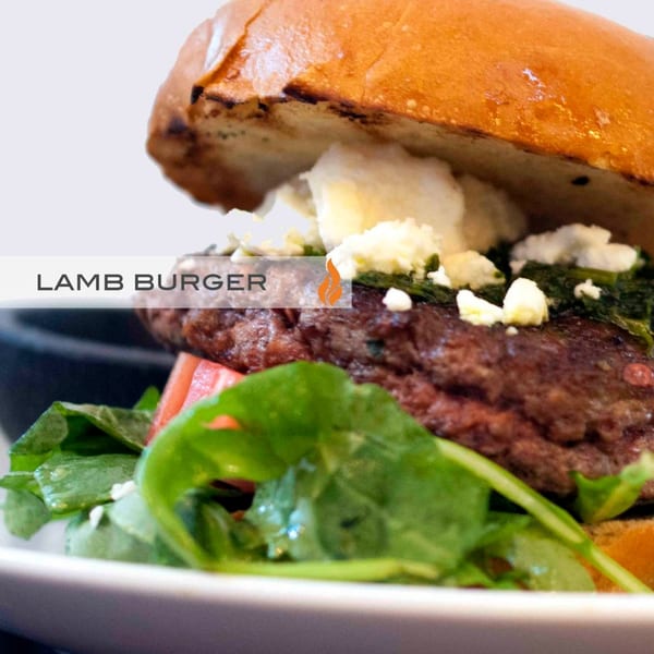 Close-up of a Byblos lamb burger with feta, spinach, and greens on a white plate.
