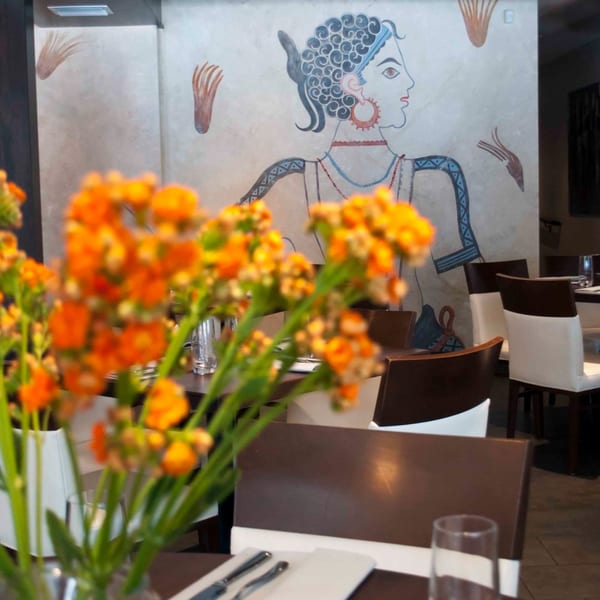 Orange flowers in the foreground, with a Mediterranean-style mural and dining tables in the background.