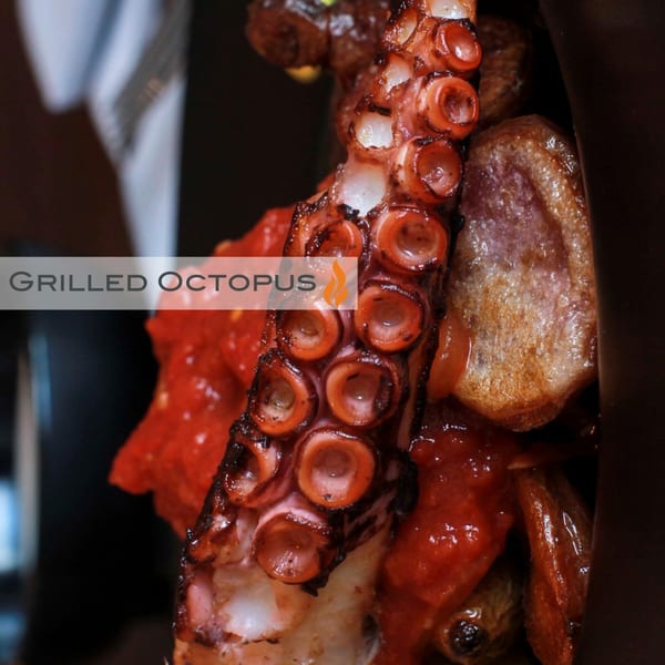 Close-up of Byblos's grilled octopus, charred and succulent, with a rich red sauce.