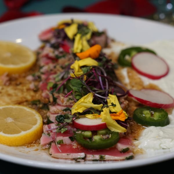 Byblos' Mediterranean tuna dish with lemon, radishes, jalapeños, and edible flowers on a white plate.