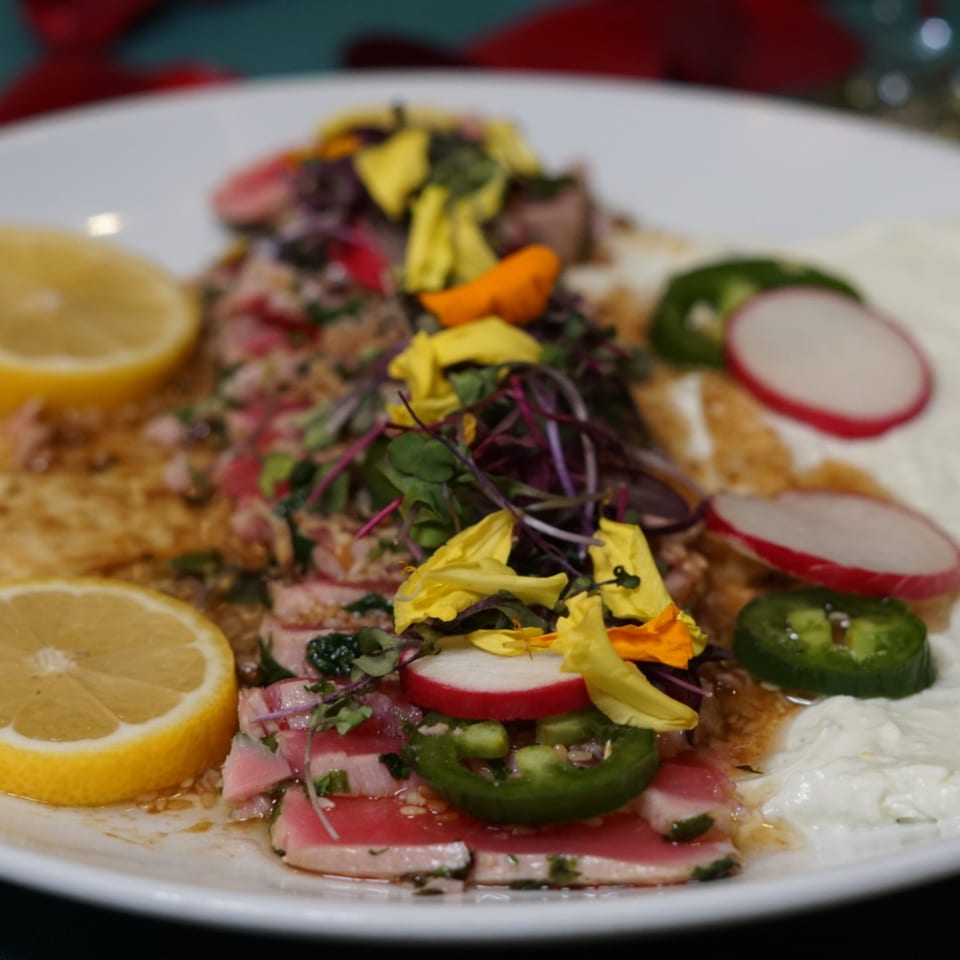 Byblos' Mediterranean tuna dish with lemon, radishes, jalapeños, and edible flowers on a white plate.