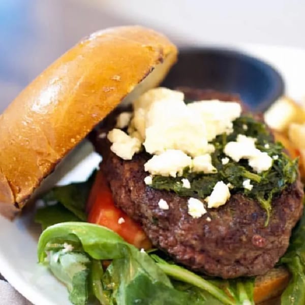 Byblos Mediterranean burger with feta, spinach, tomato, and greens on a bun.