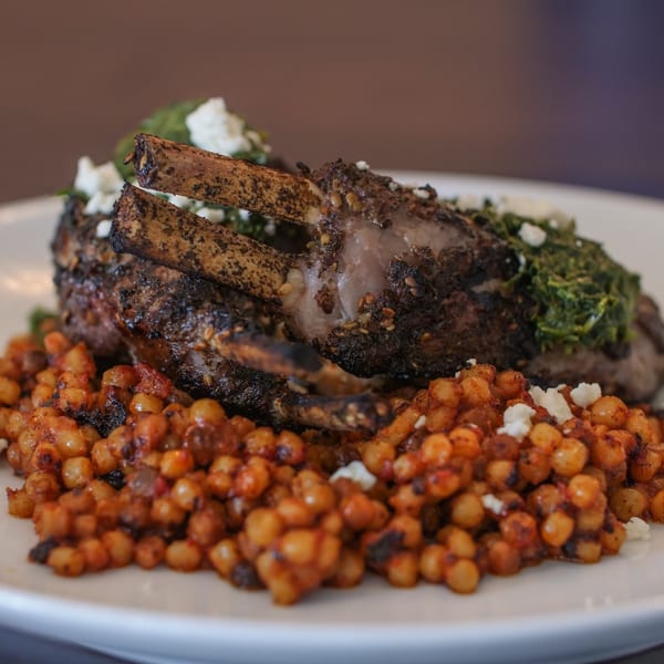 Byblos' grilled lamb chops with green herb sauce, feta, and couscous on a white plate.