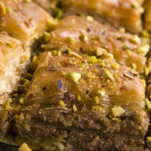 Close-up of golden baklava squares, generously topped with chopped green pistachios.