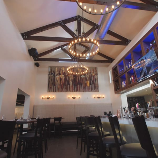 Byblos restaurant interior with high ceilings, exposed beams, circular chandeliers, and a long bar.