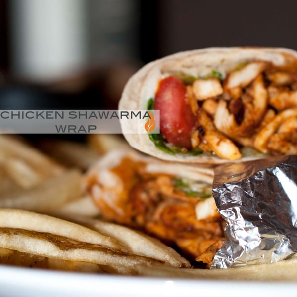 Byblos chicken shawarma wrap with tomato, greens, and fries on a white plate.