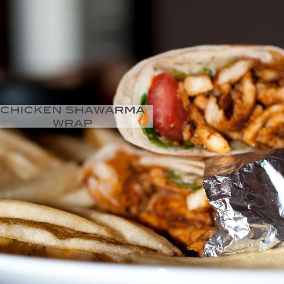 Byblos chicken shawarma wrap with tomato, greens, and fries on a white plate.