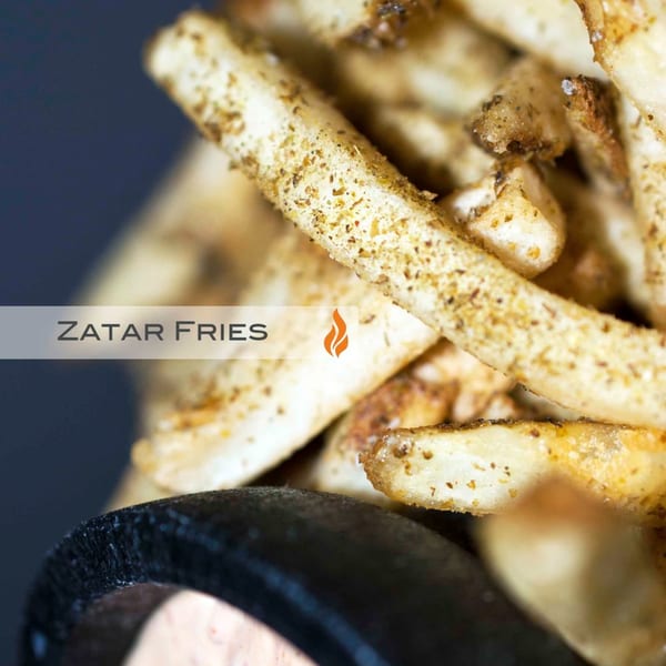 Close-up of golden-brown Zatar fries, seasoned with spices, in a dark container.