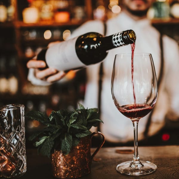 A bartender in a white shirt and suspenders pours red wine into a glass at Byblos.