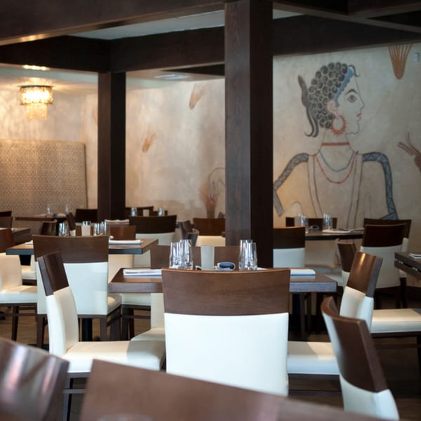 Byblos Mediterranean restaurant interior with tables, chairs, and a large mural of a woman on the wall.