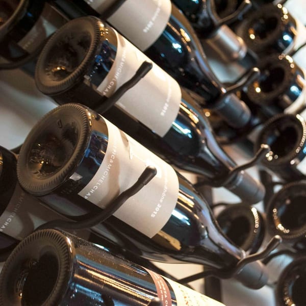 Dark wine bottles with light labels, including "MICHELCHAP" and "Rhône 2015", stored in a rack.