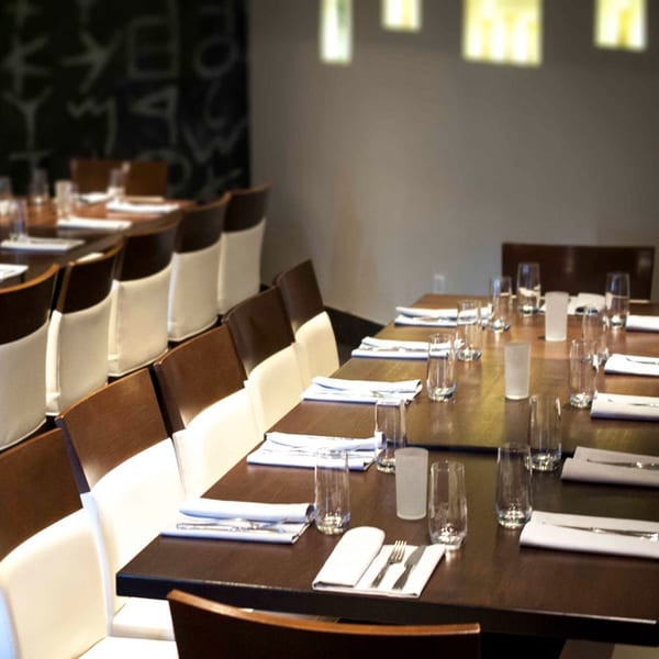 Long dining tables set with white napkins, silverware, and glasses in a Mediterranean restaurant.