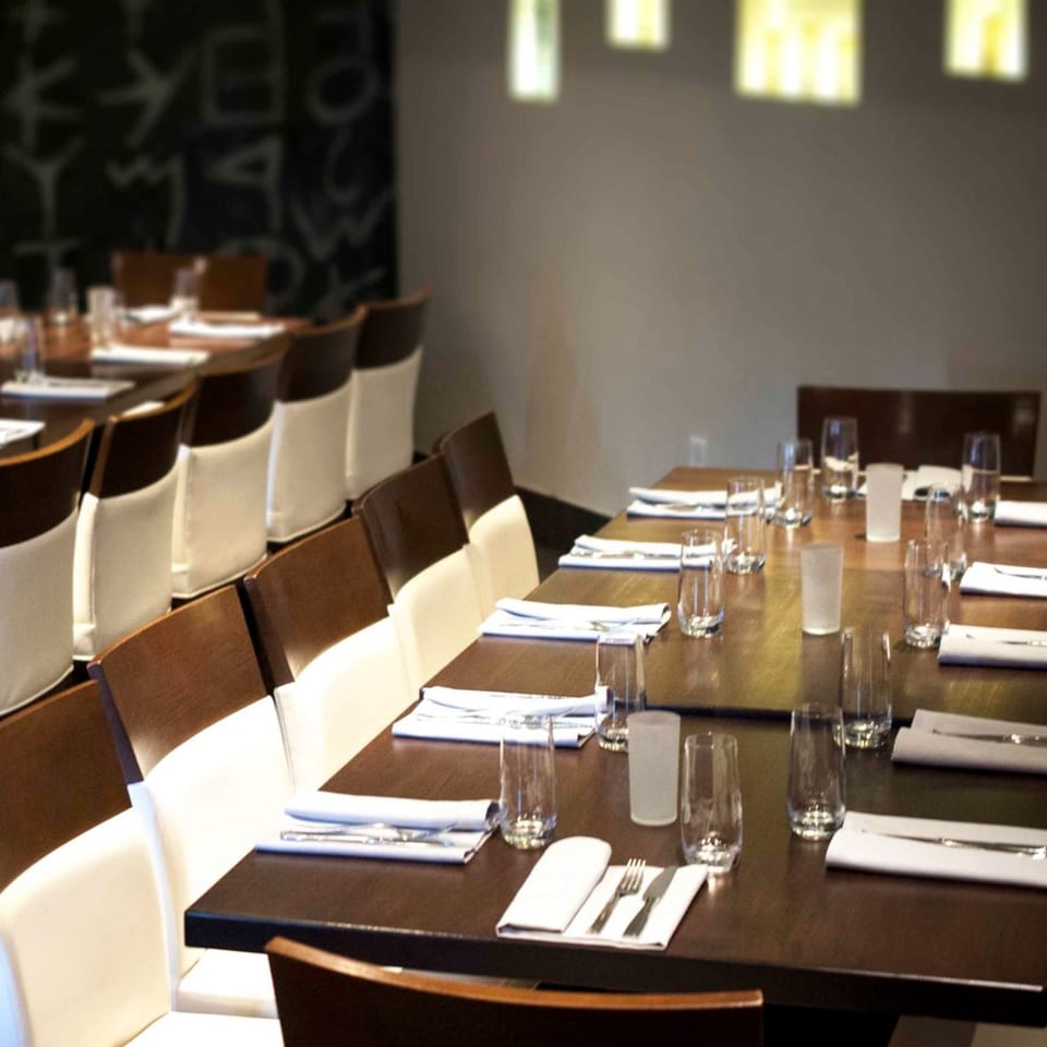 Long dining tables set with white napkins, silverware, and glasses in a Mediterranean restaurant.