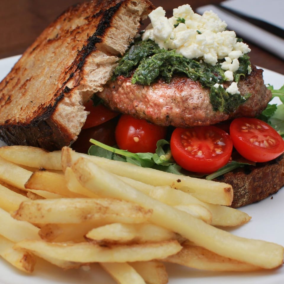 Byblos's Mediterranean burger with pesto, feta, tomatoes, and arugula, served with golden fries.