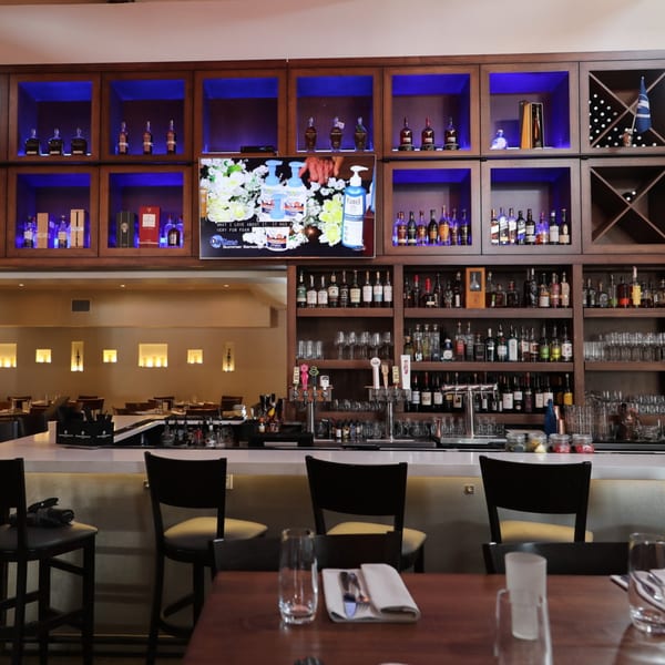 Byblos bar area with a white counter, bar stools, and shelves filled with liquor bottles.