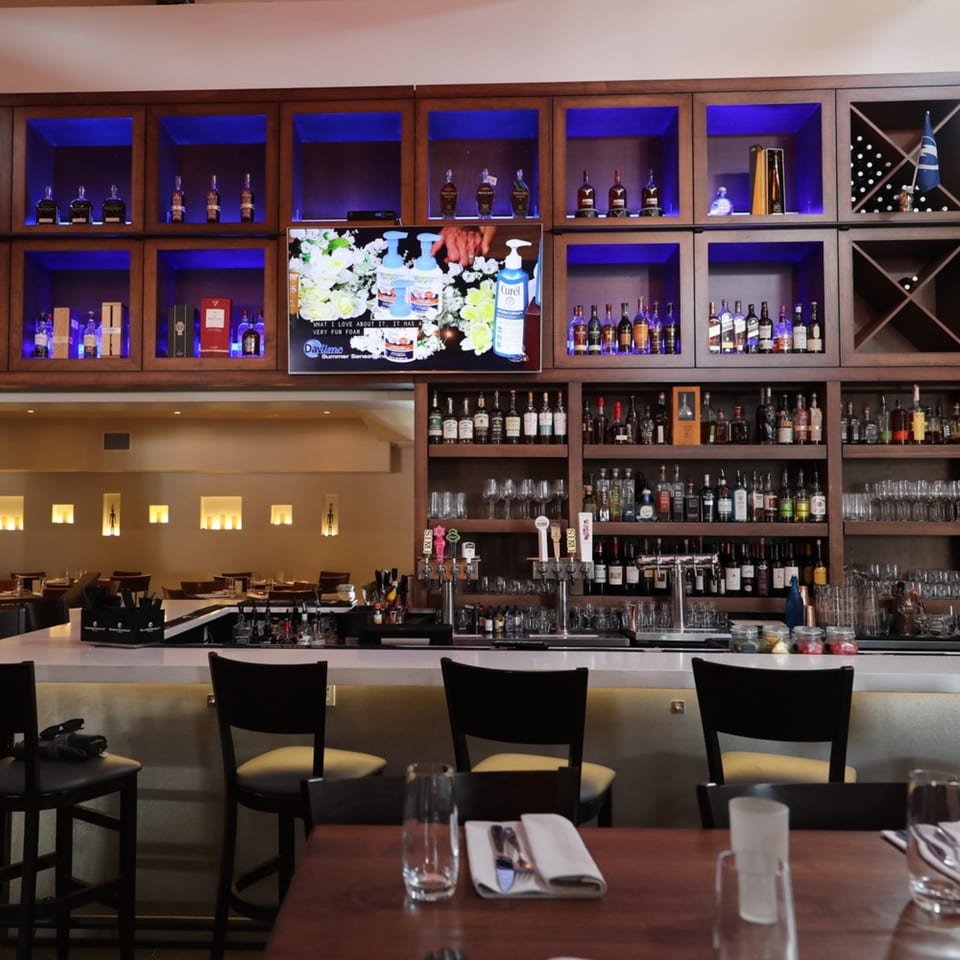 Byblos bar area with a white counter, bar stools, and shelves filled with liquor bottles.